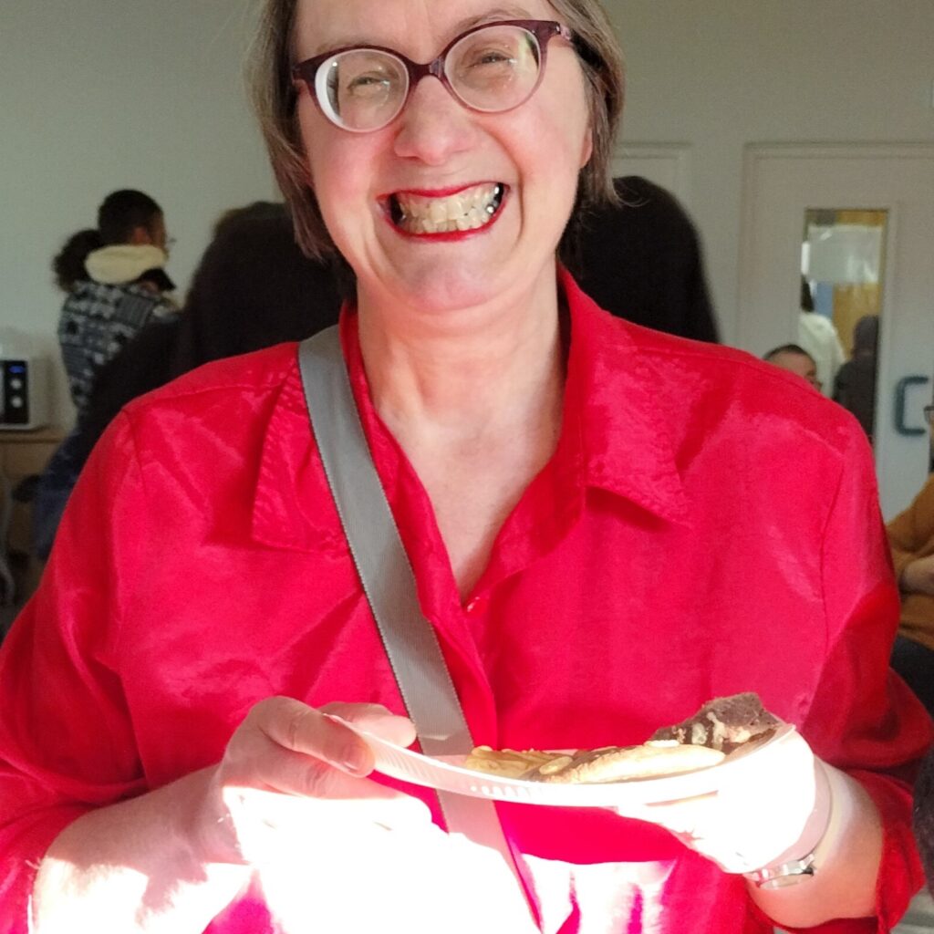 Une résidente du foyer d'hébergement tient une assiette de friandises affichant un grand sourire.